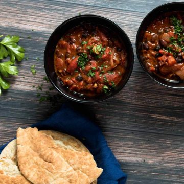 two bowls of black bean and chipotle stew served ith pita bread