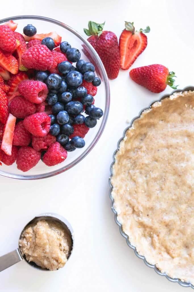 assembling a mixed berry tart, a bowl of berries and vegan pastry in a tart pan 