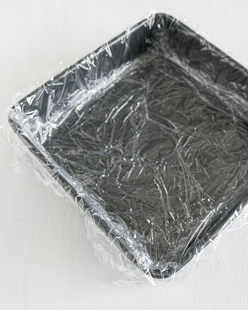 a square baking tin lned with plastic wrap for canding making