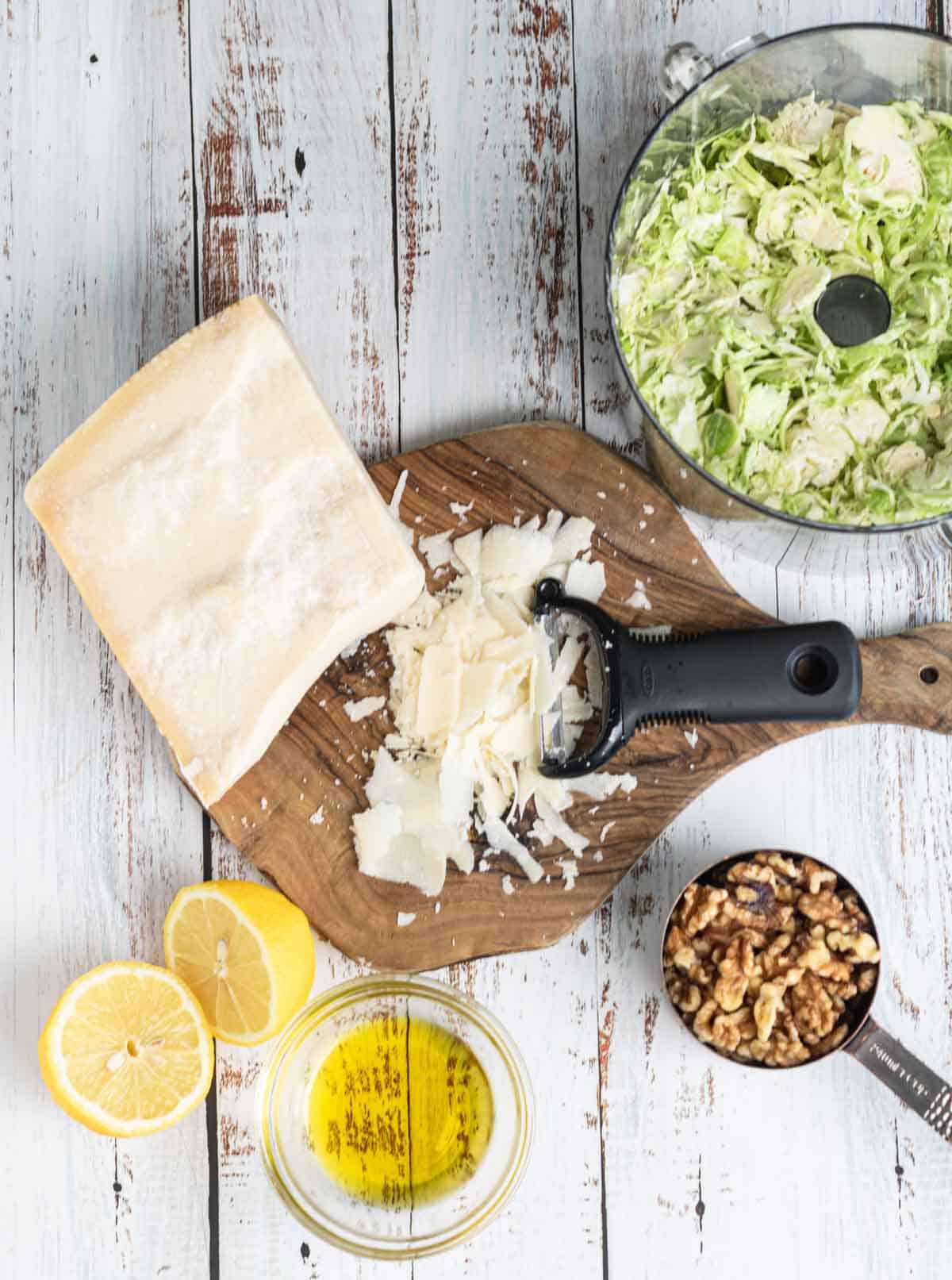 Butter, cheese, and fresh salad ingredients for a raw shaved Brussel Sprout salad on rustic wooden surface.