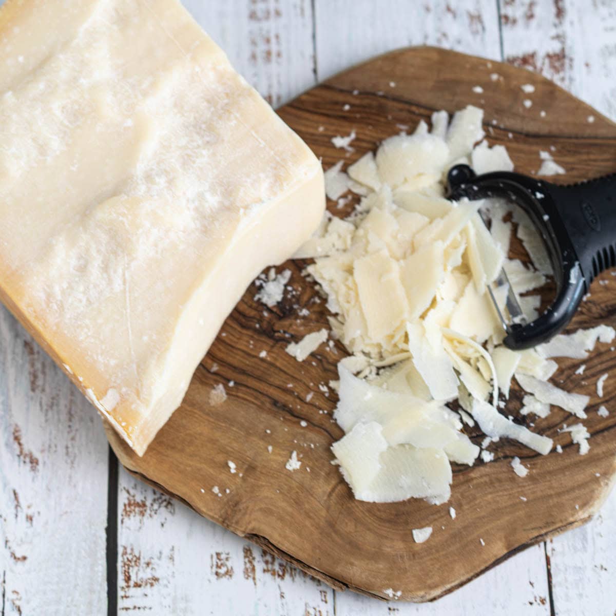 parmesan cheese block
shaved with vegetable peeler, and shavings on rustic wooden cutting board.