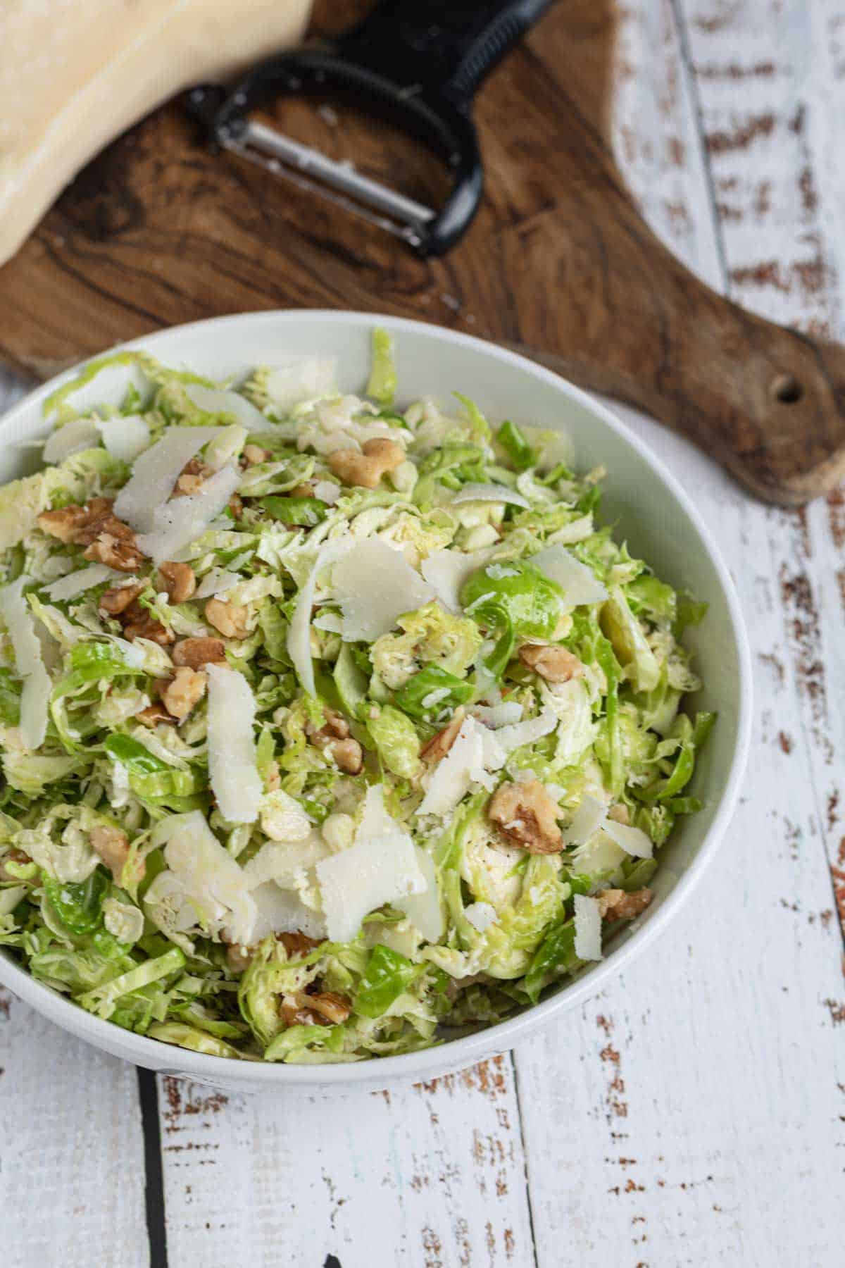 Fresh raw Brussels Sprout salad with thinly sliced Brussels sprouts, Parmesan cheese, and walnuts in a white bowl.