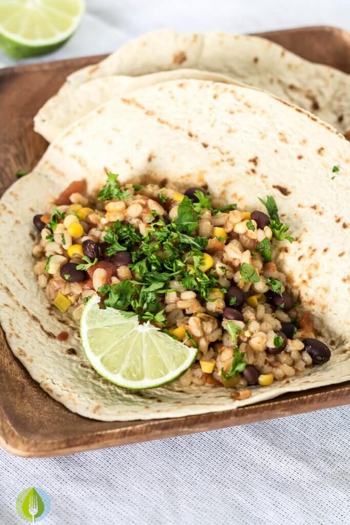 whole grain torilla filled with black bean and barley burrito filling with lime on a wood plate