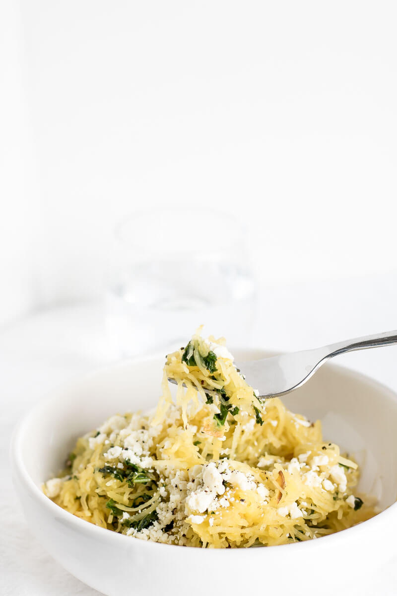 A bowl of spaghetti squash tossed with kale and feta with a fork taking a bite