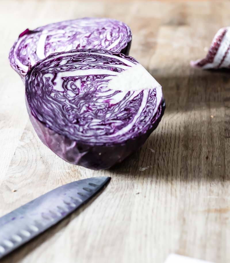 a  red cabbage cut in half on a cutting board, knife in foreground