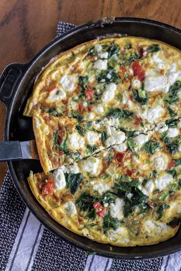 spincah frittata in a cast iron skillet with goat cheese, sliced for serving
