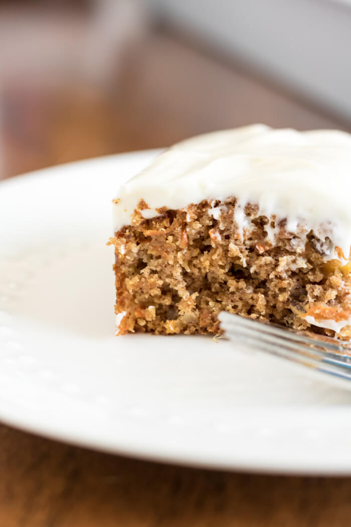 a piece of carrot cake with cream cheese frosting n a plate with a fork, 