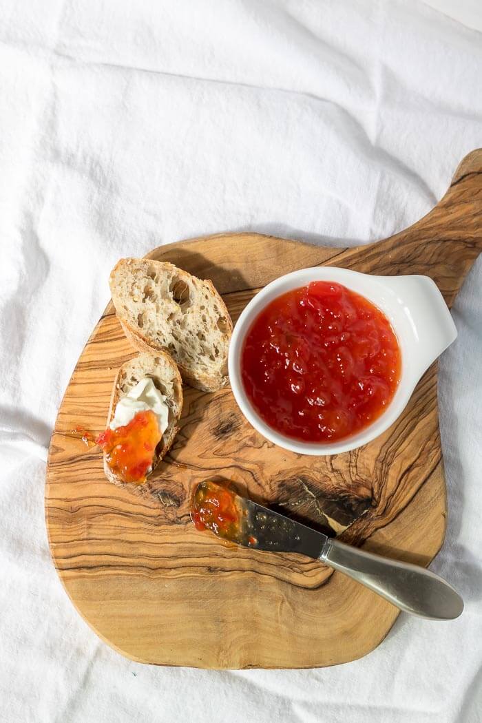top side view on jam on bread and cheese and cutting board, chili jam in a small white bowl