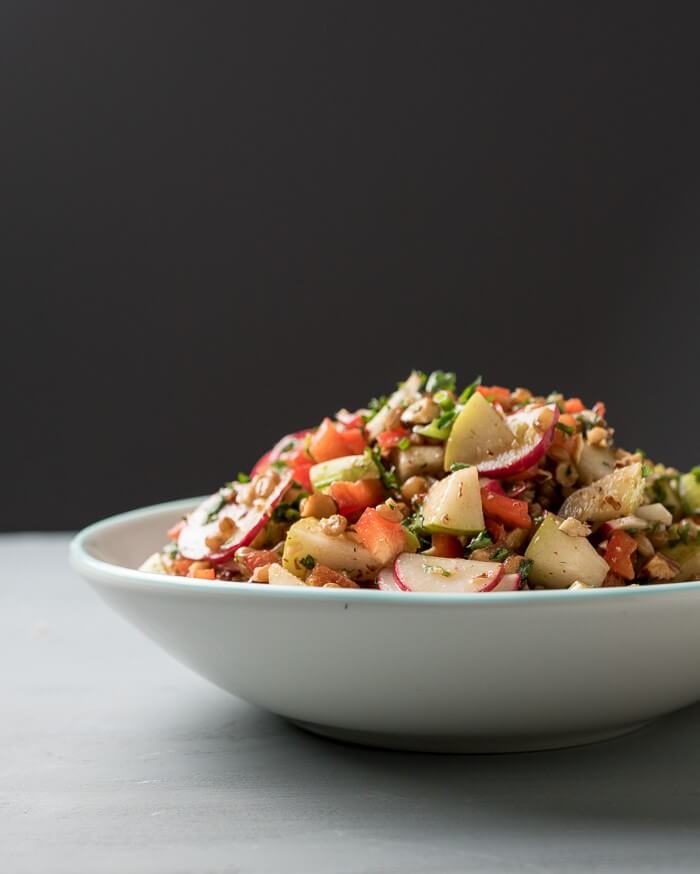 wheat berry salad with almonds, pears, radish iand parsley n a white bowl and black background