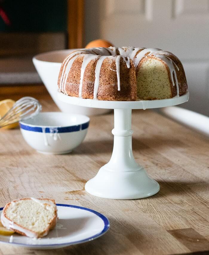 poppyseed lemon cake with lemon frosting on a cake stand with glaze in the background
