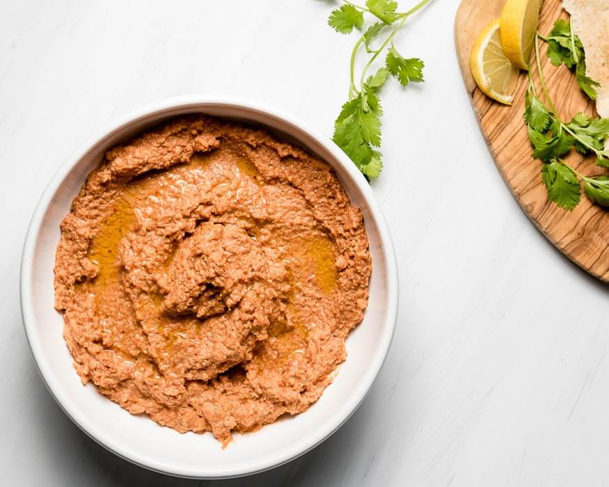 Muhammara Roasted Red Pepper spread in a white bowl spread  with lemon and cilantro on a wooden cutting board