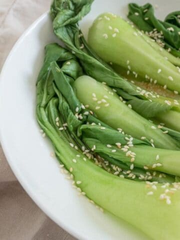 steamed boy choy with sesame seeds on a white plate