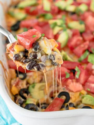 vegetarian taco bake with black beans, cheese and avocado, spoon is scooping cheesy taco bake from casserola