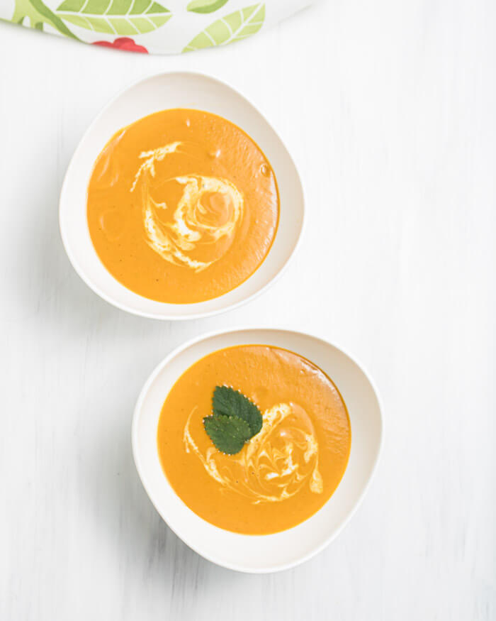 two bowls a of curried carrot soup with coconut milk swirled, garnished with a mint leaf