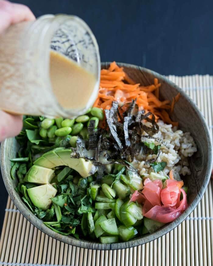 pouring miso dressing over sushi lunch bowls