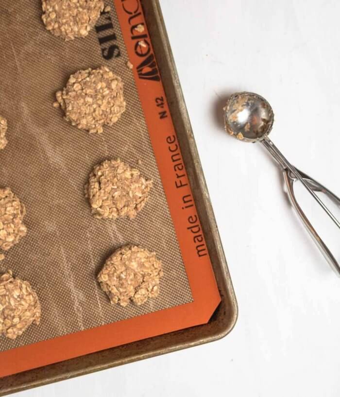 giant vegan oatmeal granola cookies ready to bake on  baking tray lined with silpat and a large cookie scoop