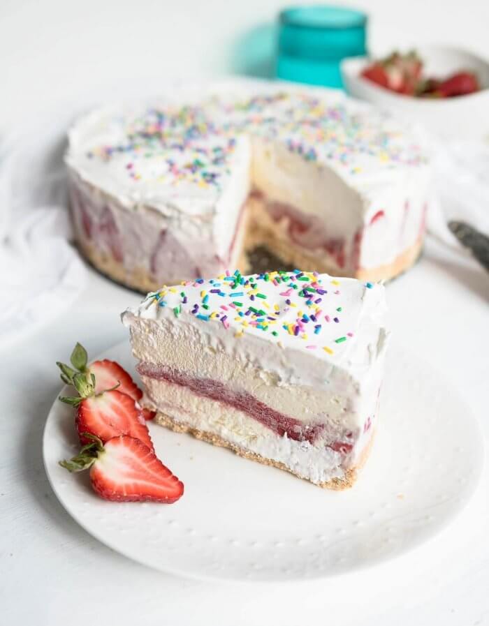 a slice of vanilla ice cream cake with strawberries with whole cake in background