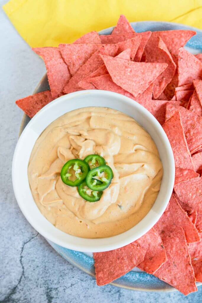 vegan queso dip surrounded by red nacho chips with jalapenos