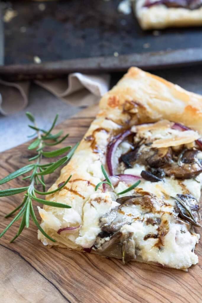 wild mushrrom and goat cheese pizza made with puff pastry on serving platter with rosemary and balsamic drizzle