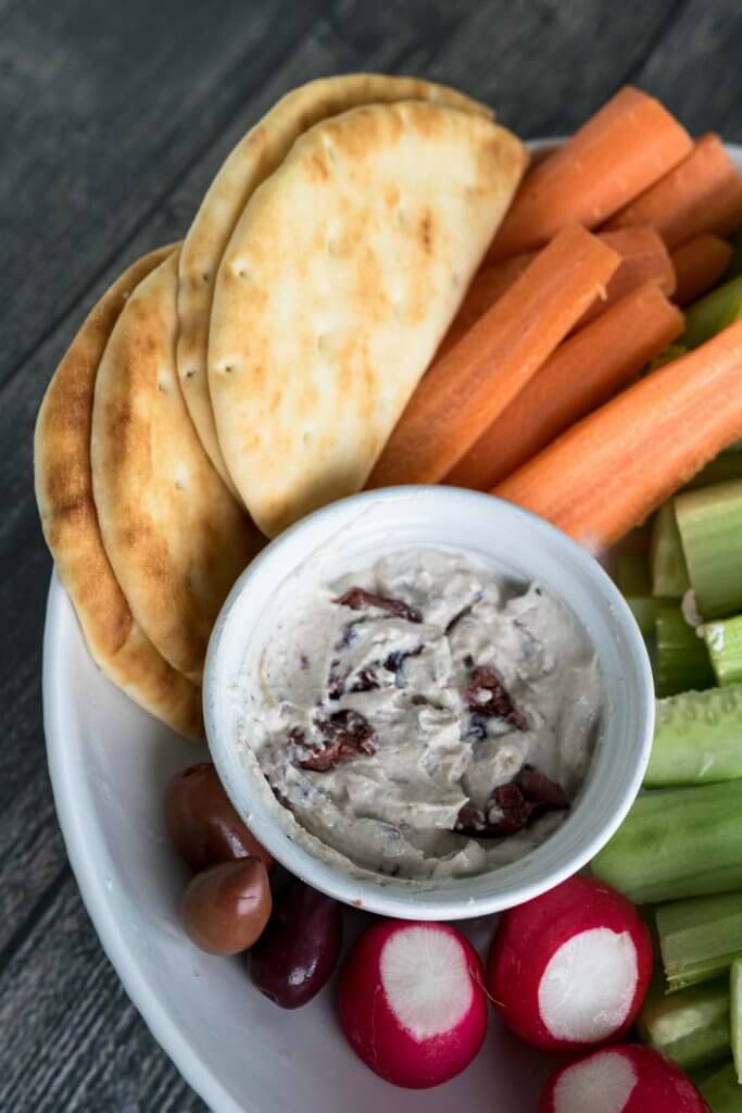 tahini and greek yogurt tip with olive on a platter with pita and fresh vegetables for dipping