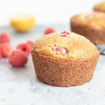 side view of raspberry and poppy seed muffin, fresh raspberries in background