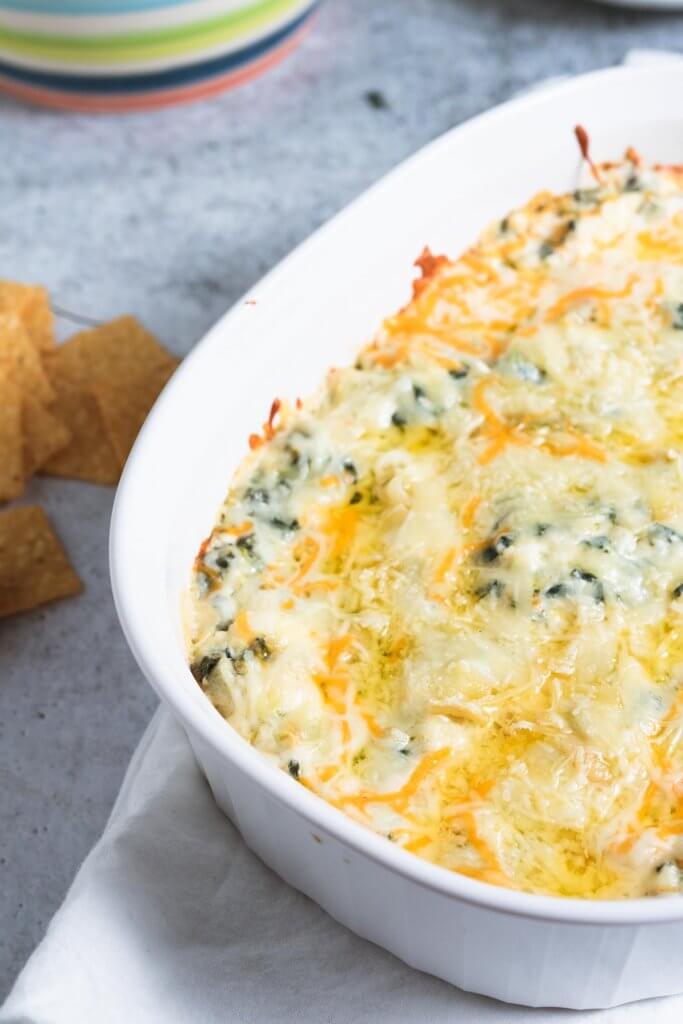 hot artichoke dip with spinach and melted cheese on top in a white casserole dish