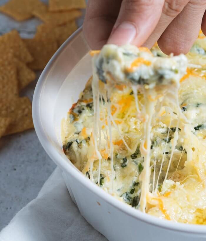 a chip dipping into a hot and cheezy spinach and artichoke dip