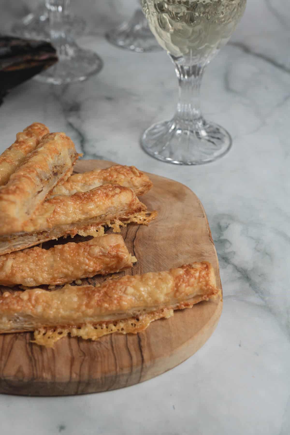 Crispy, homemade cheese straws on a wooden serving board, wine glass in background, marble surface, recipe for entertaining at home, New Year's Eve, appetizers