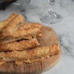 Crispy, homemade cheese straws on a wooden serving board, wine glass in background, marble surface, recipe for entertaining at home, New Year's Eve, appetizers