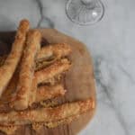 Crispy cheese sticks with marinara sauce on wooden serving tray and glass of white wine in the background, perfect appetizer.