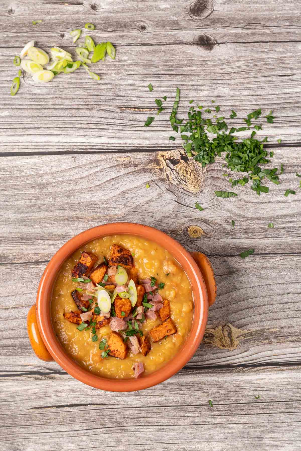 split pea soup with ham and roasted sweet potatoes in a terracotta bowl and garnished with parsley and green onions