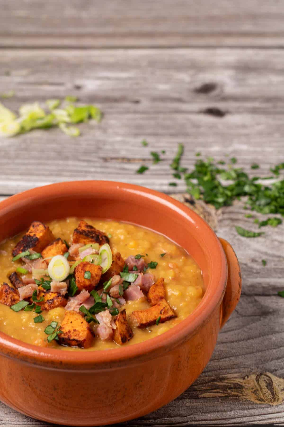 split pea soup with ham and roasted sweet potatoes in a terracotta bowl and garnished with parsley and green onions