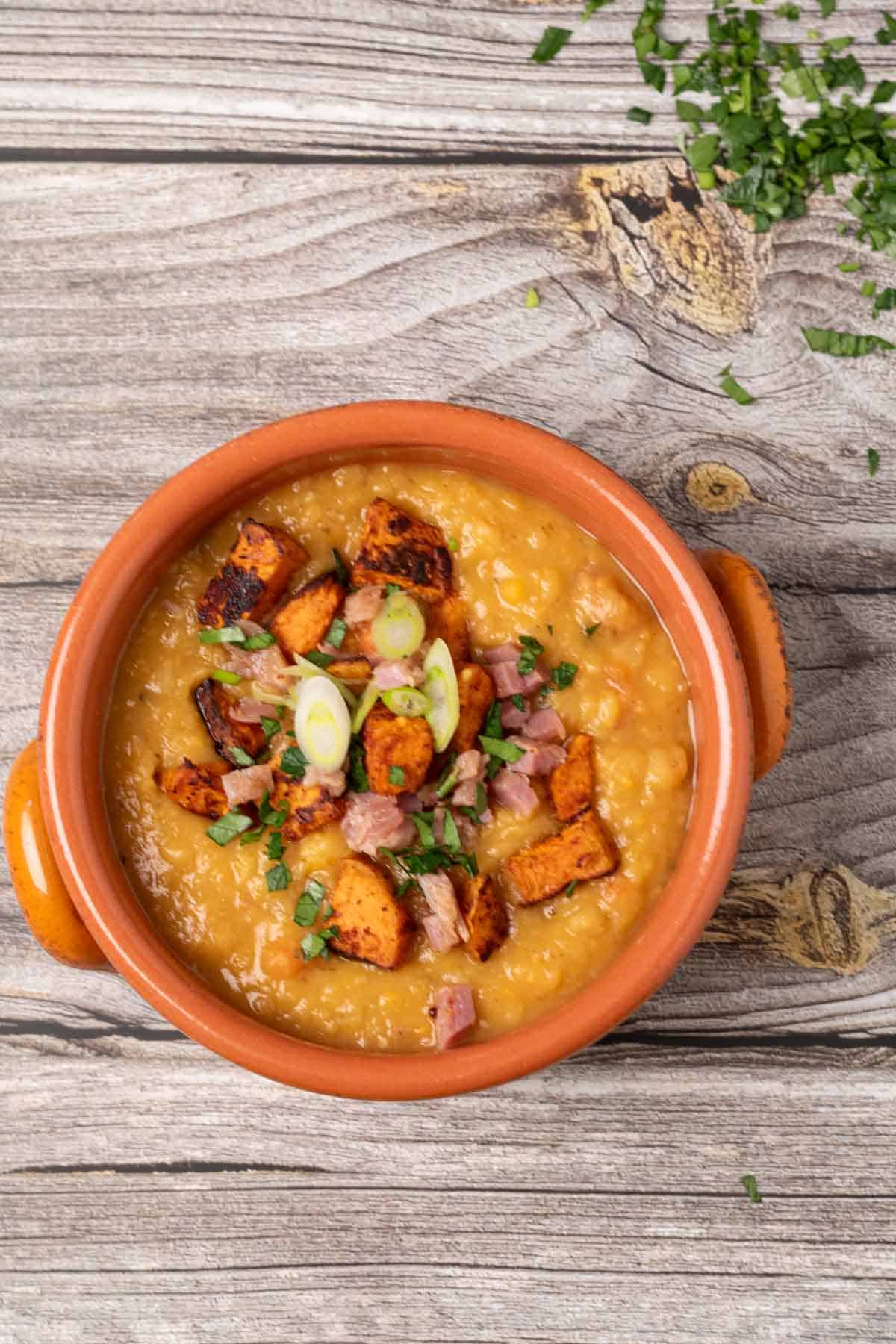 split pea soup with ham and roasted sweet potatoes in a terracotta bowl and garnished with parsley and green onions