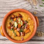 split pea soup with ham and roasted sweet potatoes in a terracotta bowl and garnished with parsley and green onions