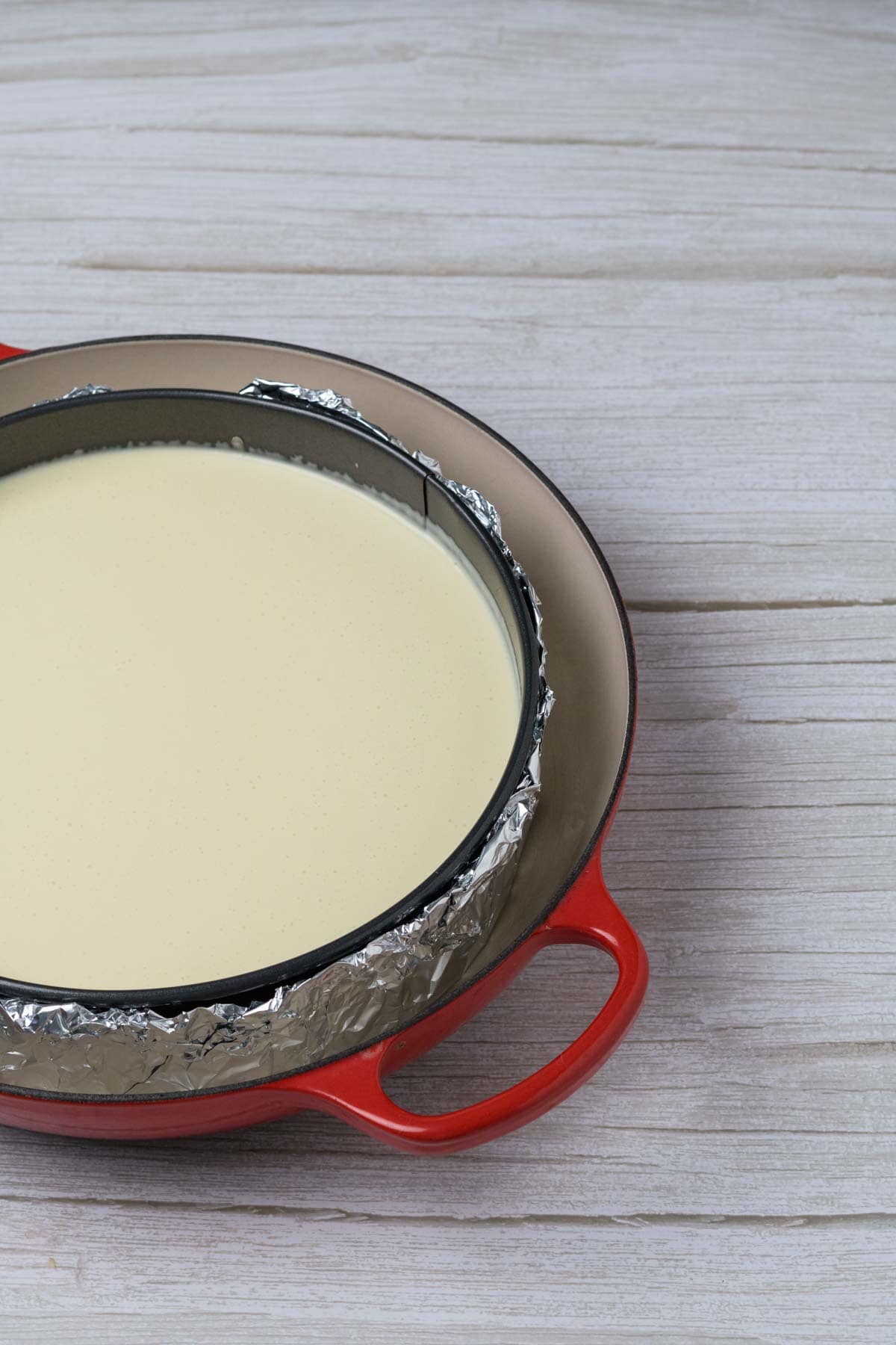 almond cheesecake in a spring form pan wrapped in foil and set in a water bath ready for baking