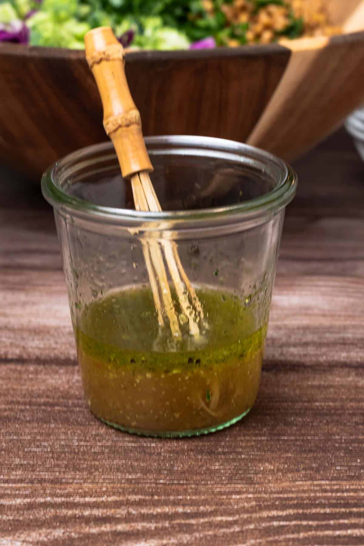 apple cider and maple dressing in a small glass jar with bamboo whisk