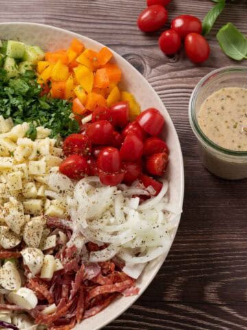 chopped italian salad with ingredients on a serving platter ready to be tossed, salami, provolone, tomatoes